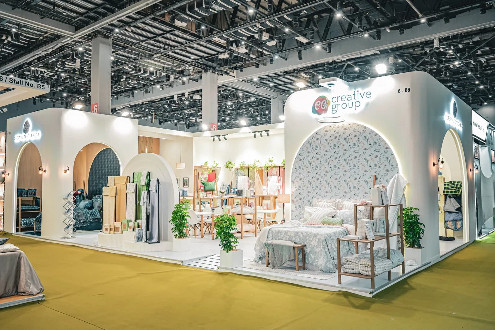 A stand built from a run of white arches on a yellow-green floor, each arch framing a bay of textile samples.