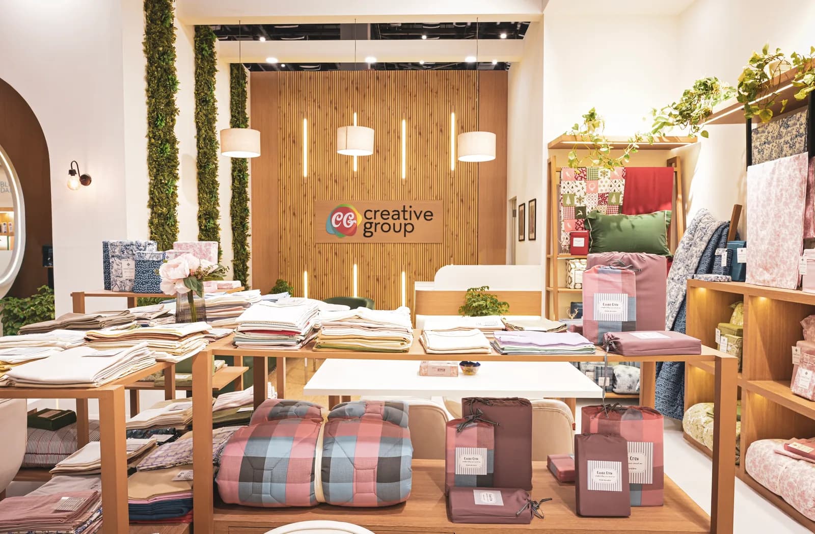 The Creative Group stand: timber panelling and planting behind a long table laid with folded fabric, cushions and swatch books.