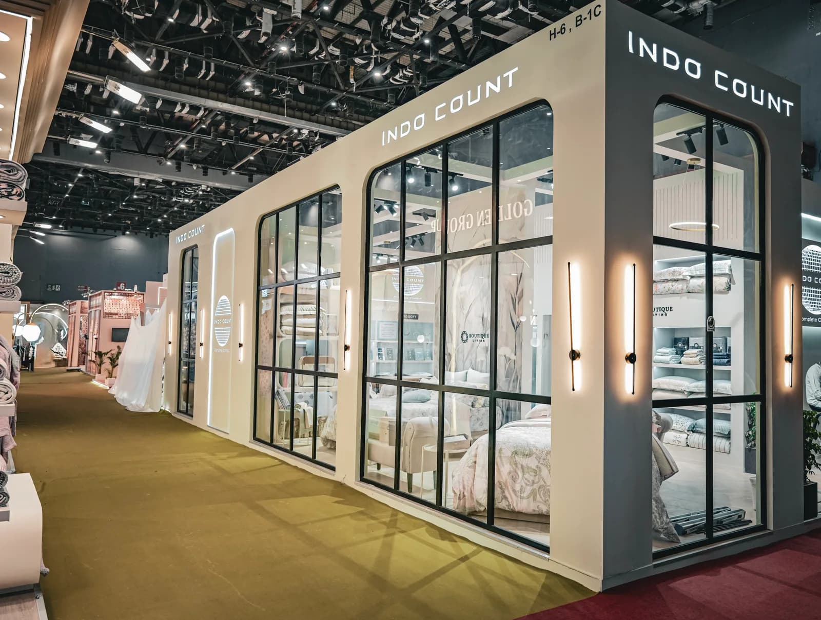 The Indo Count stand: a long white facade of glazed steel doors under the name in black, with bedding displays visible through the glass.