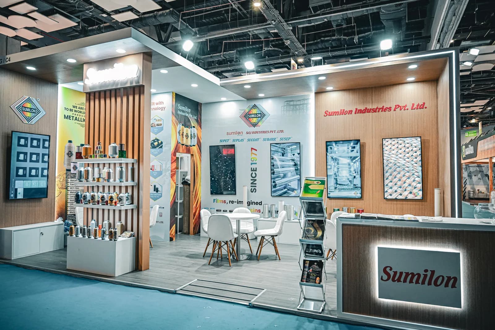 The Sumilon Industries stand: a product wall of framed samples, a slatted timber ceiling and a white meeting table with chairs.