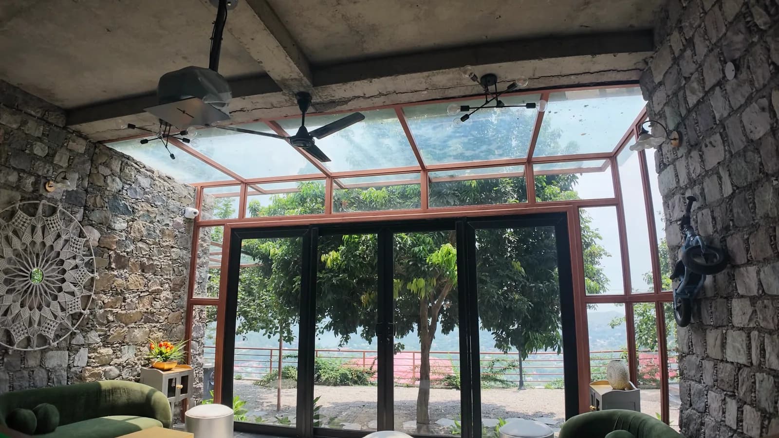 A stone-walled room opening through full-height glazed doors onto planting and the valley beyond.
