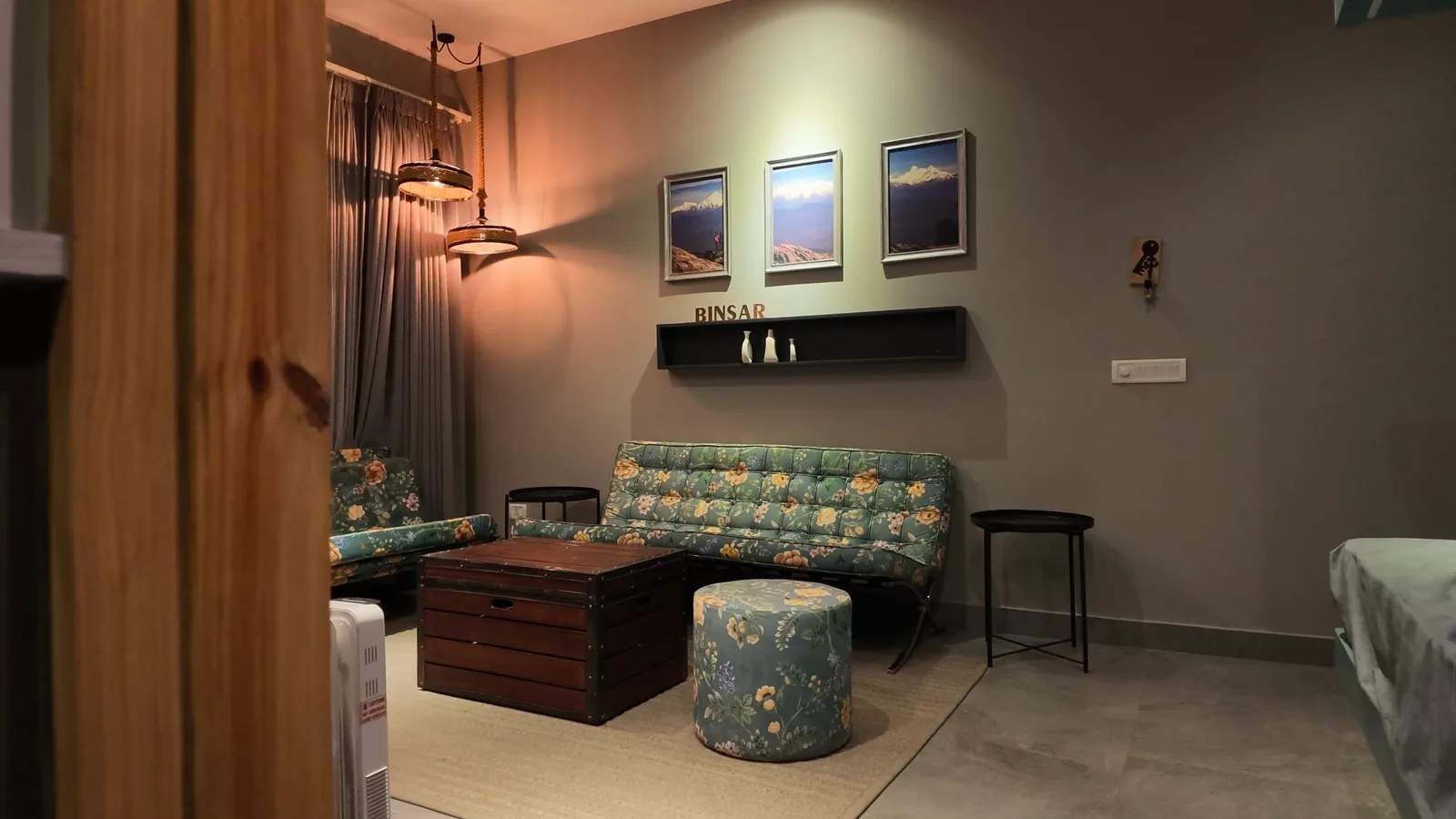 A lounge with a patterned sofa, a wooden trunk for a table and a framed television on a pale wall.