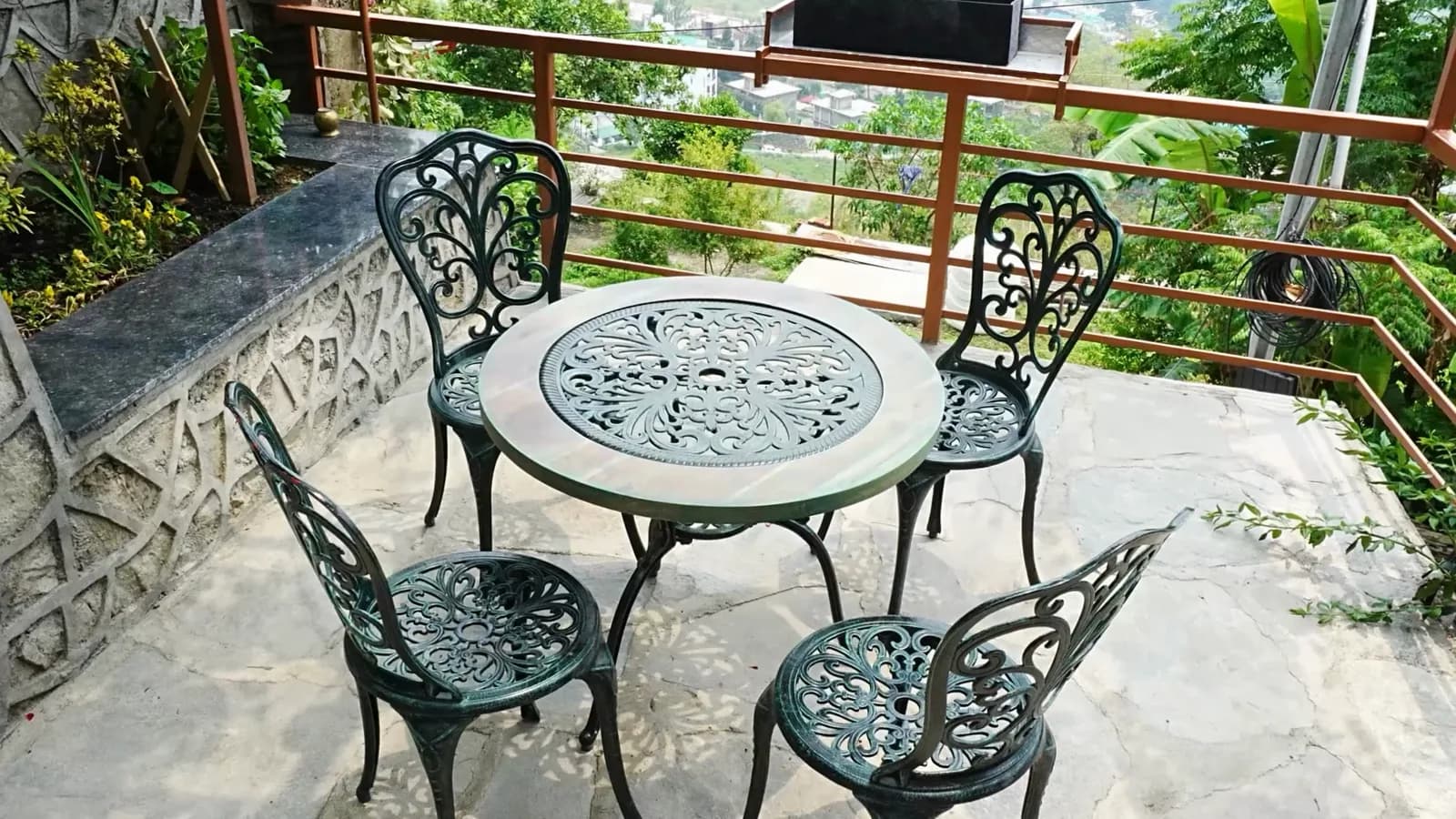 A wrought-iron table and two chairs on a stone terrace, planting spilling over the low wall behind them.