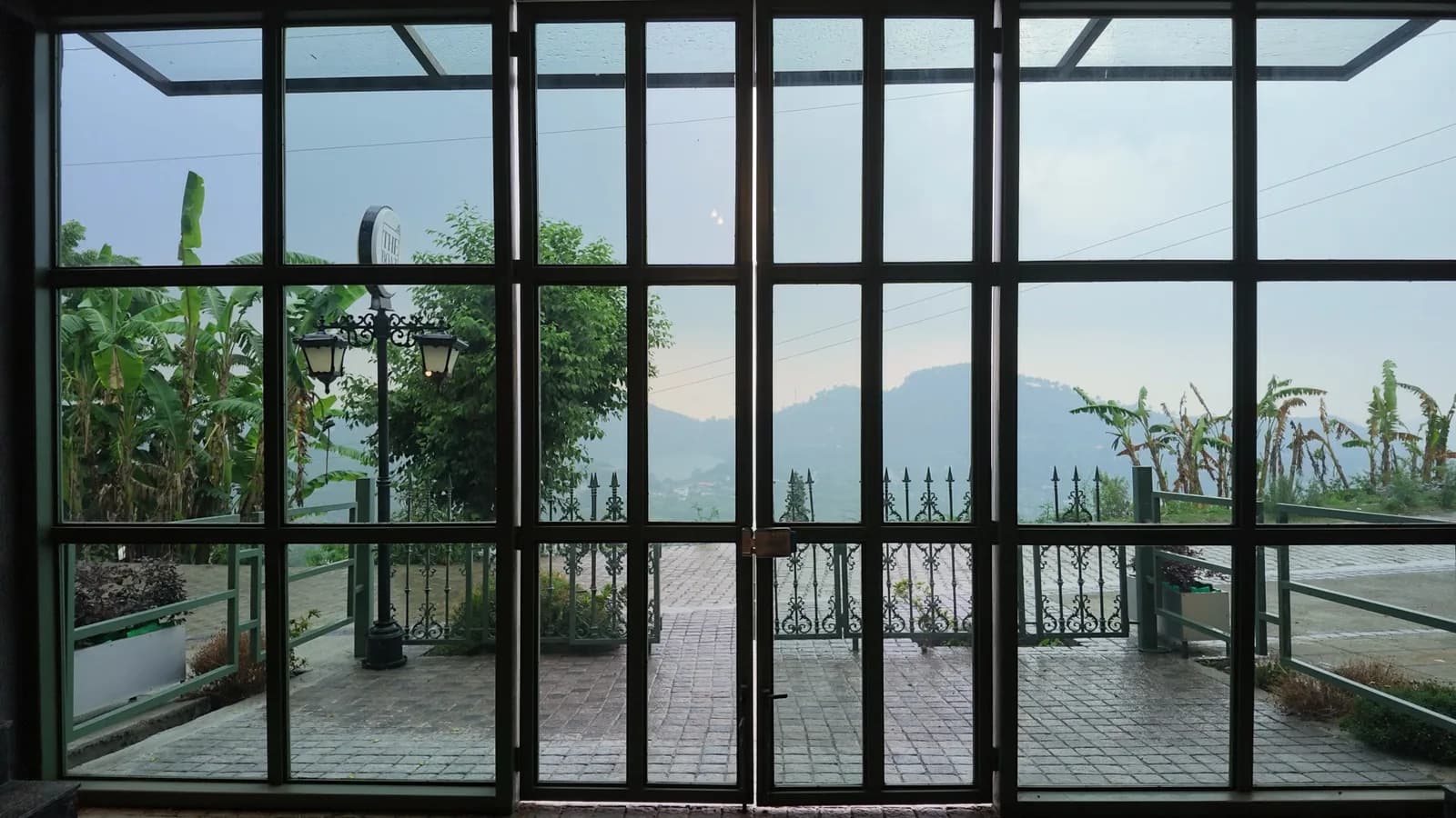 A black steel-framed glazed wall running the length of a room, looking out over the hills.
