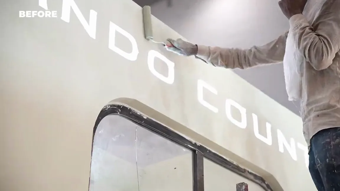 The before and after cut: a worker painting the Indo Count name onto a bare panel, then the same stand finished, with lit shelving, folded stock and a fitted meeting room.