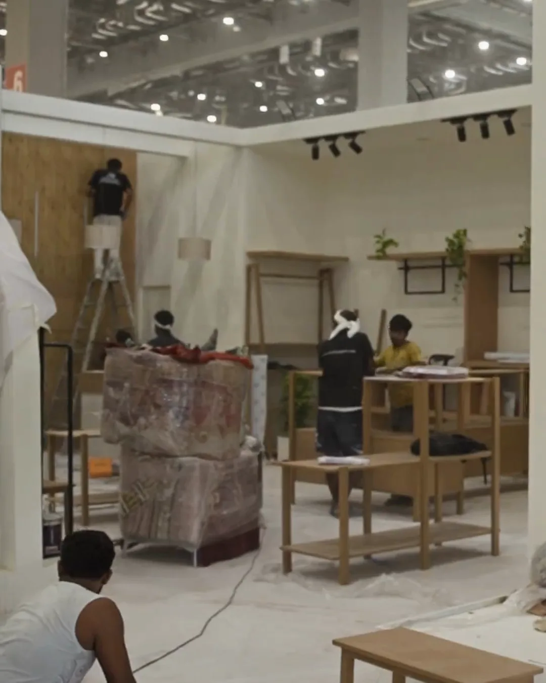 The build in progress: ladders against half-finished walls, panels being carried in, a floral print being hung, and crates still open on the floor.